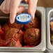 A hand using a Comark 300 digital pocket probe thermometer to check the temperature of meatballs.