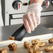 A hand in a plastic glove using Tablecraft black silicone-coated tongs to serve food.