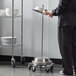 A person in a black uniform using an American Metalcraft aluminum plate cover cart to transport dishes.