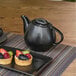 A Front of the House black porcelain teapot on a table with fruit tarts.