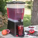 A Carlisle black polypropylene base holding a juice dispenser with red liquid and ice with a cherry on a black surface.