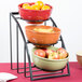 A black Cal-Mil bowl display stand holding three bowls of fruit.