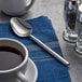 An Acopa stainless steel teaspoon on a blue napkin next to a cup of coffee.