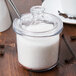 A glass Cambro condiment jar with a slotted lid full of sugar with a spoon.