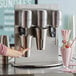 A person using an AvaMix milkshake machine to pour a drink into a silver metal cup.
