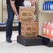 A man using a Regency black plastic case stacker to hold boxes in a store.