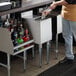 A man standing at a stainless steel underbar ice bin with a tray of drinks.