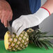 A person wearing San Jamar cut-resistant gloves cutting a pineapple.