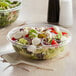 A Dart Clear OPS plastic bowl filled with salad on a white surface.