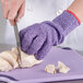 A person cutting meat with a San Jamar purple cut resistant glove.