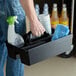 A man holding a black Rubbermaid Executive divided carry caddy with cleaning supplies on a counter.