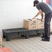A man placing boxes on a black plastic Regency dunnage rack.