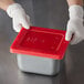 A person wearing gloves holding a red lid for a Vollrath steam table pan.