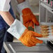 A person wearing Matfer Bourgeat orange leather gloves holds a tray of cookies.