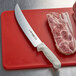 A Dexter-Russell cimeter steak knife on a cutting board next to a piece of meat.