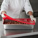 A woman in a white chef's coat using a Vollrath red flexible steam table lid to cover a tray of meatballs.