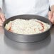 A person using an American Metalcraft Hard Coat Anodized Aluminum pan to bake a pizza.
