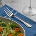 An Acopa Lydia stainless steel salad fork on a napkin next to a bowl of salad.