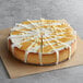 A Pellman lemon cheesecake with white frosting and white and yellow toppings on a bakery display table.