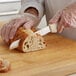 A person in a plastic glove using a Dexter-Russell white scalloped bread knife to cut bread.