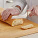 A person in white gloves using a Dexter-Russell scalloped bread knife to cut a loaf of bread.