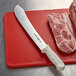 A Dexter-Russell Sani-Safe butcher knife on a cutting board next to meat.