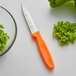 A Dexter-Russell paring knife with an orange handle next to a bowl of chopped green peppers.