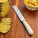 A Dexter-Russell Sani-Safe vegetable knife next to a bowl of pineapple chunks.