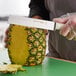 A person using a Dexter-Russell produce knife to cut a pineapple.