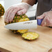 A person using a Dexter-Russell purple chef knife to cut a pineapple.