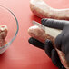 A person in black gloves using a Dexter-Russell Frankfurt skinner to cut raw sausages.