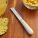 A Dexter-Russell Sani-Safe produce knife next to a bowl of pineapple chunks.