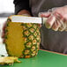 A person using a Dexter-Russell vegetable knife to cut a pineapple.