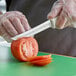 A person using a Dexter-Russell scalloped utility knife to cut a tomato.