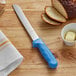 A Dexter-Russell Sani-Safe bread knife with a blue handle cutting bread.