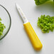 A Dexter-Russell yellow-handled paring knife with chopped green peppers.