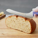 A person cutting a loaf of bread with a Dexter-Russell purple scalloped bread knife.