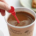 A hand holding a Royal Paper red plastic beverage stirrer in a cup of coffee.