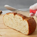 A person using a Dexter-Russell red scalloped bread knife to cut bread.
