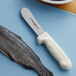 A Dexter-Russell Sani-Safe slimming knife next to a fish on a cutting board.