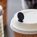 A black Royal Paper STIRSTIX-BK beverage plug clipped to a white coffee cup lid.