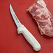 A Dexter-Russell Sani-Safe narrow curved boning knife with a white handle next to a piece of meat.