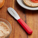 A Dexter-Russell scalloped sandwich spreader with a red handle on a table.