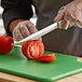 A person using a Dexter-Russell Sani-Safe scalloped utility knife to slice a tomato on a cutting board.