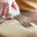 A person using a Dexter-Russell bread scoring knife to cut dough.