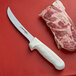 A Dexter-Russell Sani-Safe stiff boning knife next to a piece of meat on a cutting board.