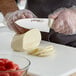 A person using a Dexter-Russell scalloped chef knife to cut cheese.