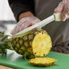 A person using a Dexter-Russell Sani-Safe scalloped utility slicer to cut a pineapple.
