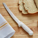 A Dexter-Russell scalloped bread knife cutting bread on a wooden cutting board.