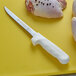 A Dexter-Russell Sani-Safe flexible boning knife next to a piece of chicken.
